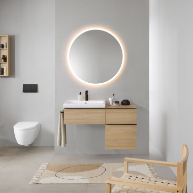 Ванна кімната із сірими стінами, дерев’яними меблями Geberit і круглим дзеркалом із підсвіткою Geberit Option