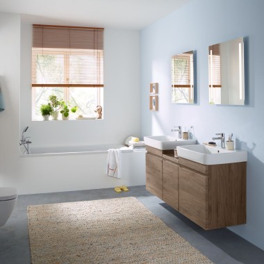 Сімейна ванна кімната зі світло-блакитною стіною та меблями для ванної кімнати з горіха, дзеркальною шафою, змивною клавішею та керамікою від Geberit